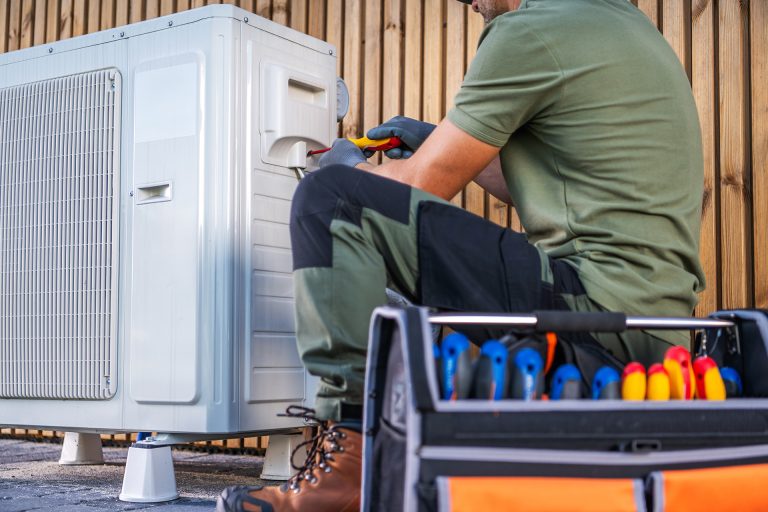 A technician is working on servicing an outdoor air conditioning unit, using various tools and equipment in a residential setting.